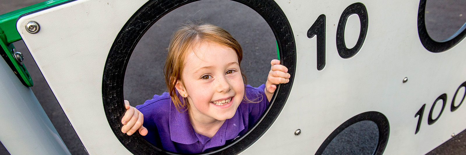 A girl is looking through an aperture on a target panel smiling.